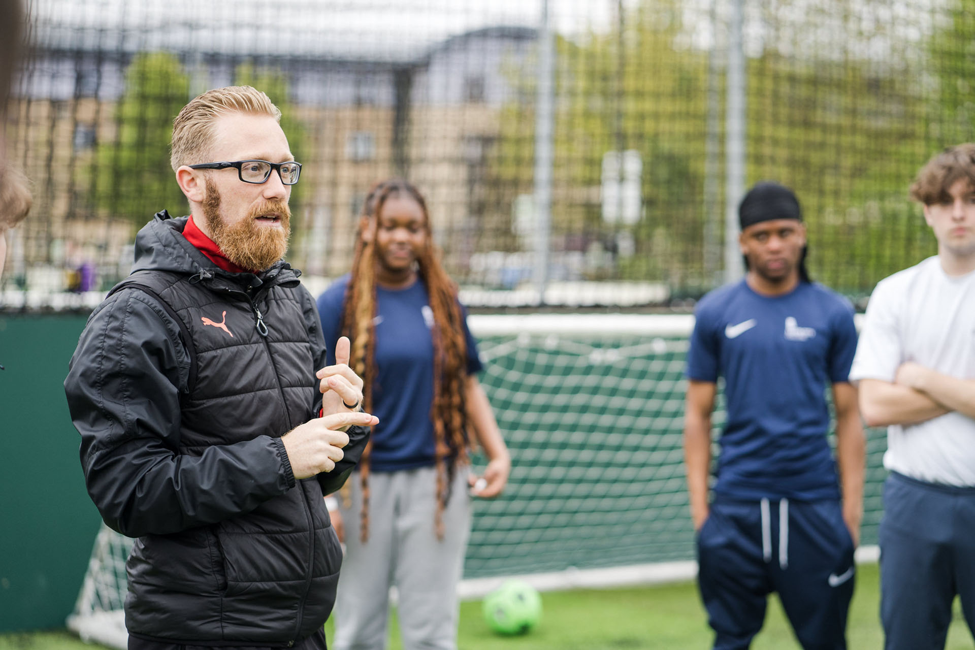 A sports teachers giving a talk to potential students out on the playing grounds