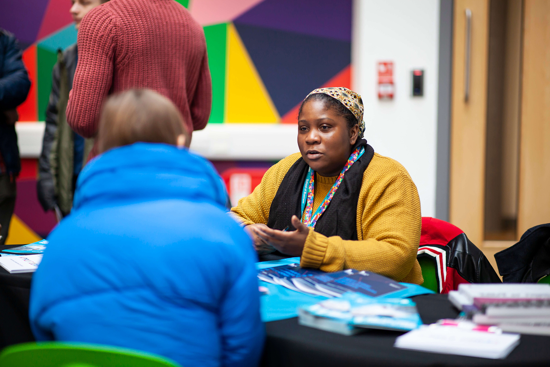 A Leeds City College tutor explaining to a prospective student about the course she teaches at an open event, there are posters, leaflets and prospectuses on the table