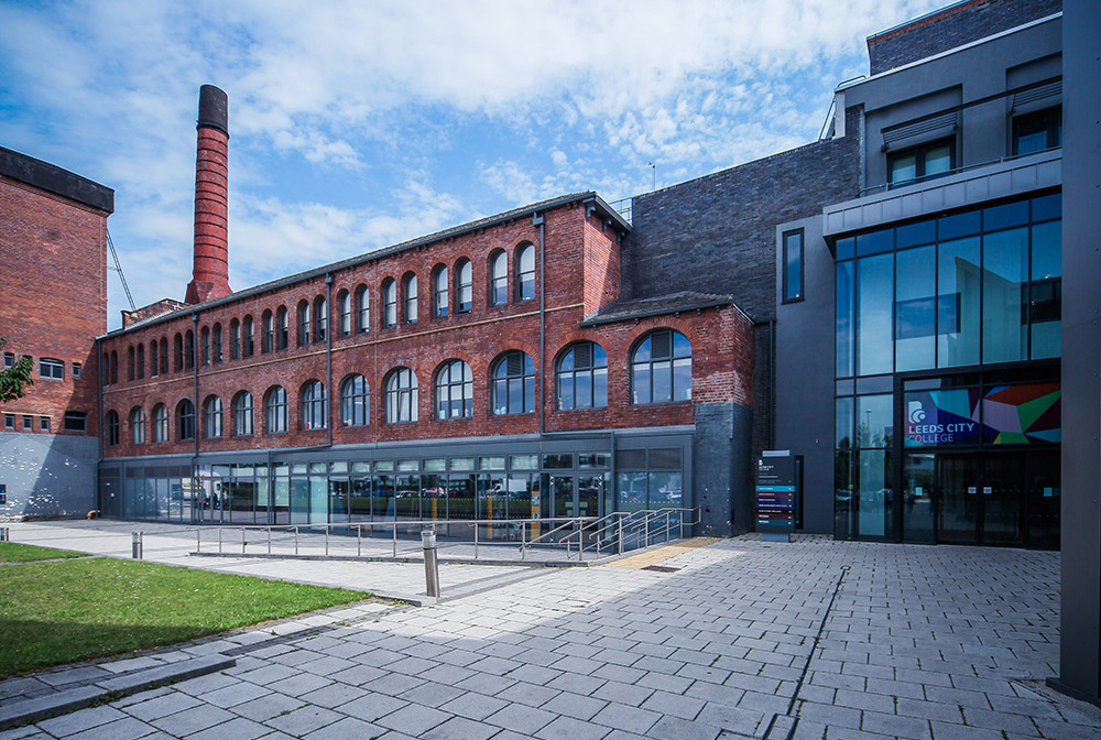 A shot of the Printworks buildings showing the new build with the old printing hall and the outside yard and grass with blue skies and white clouds