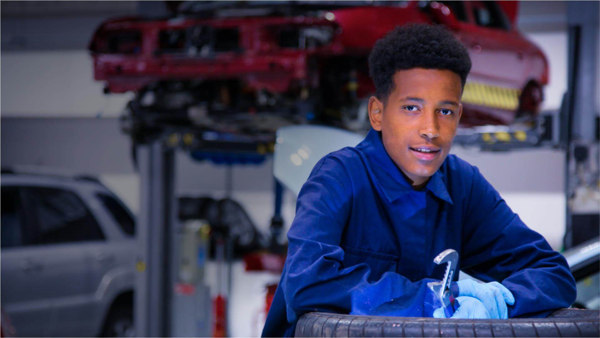 Engineering student wearing blue overalls holding a wrench looking at the camera