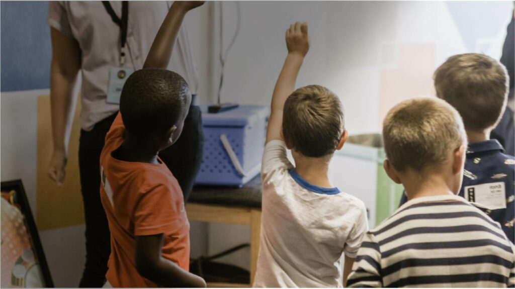 Class of children raising their hand to answer the teacher