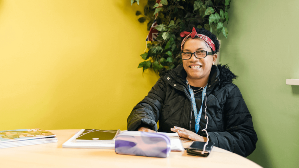 Adult student sat at desk, smiling and wearing a college lanyard