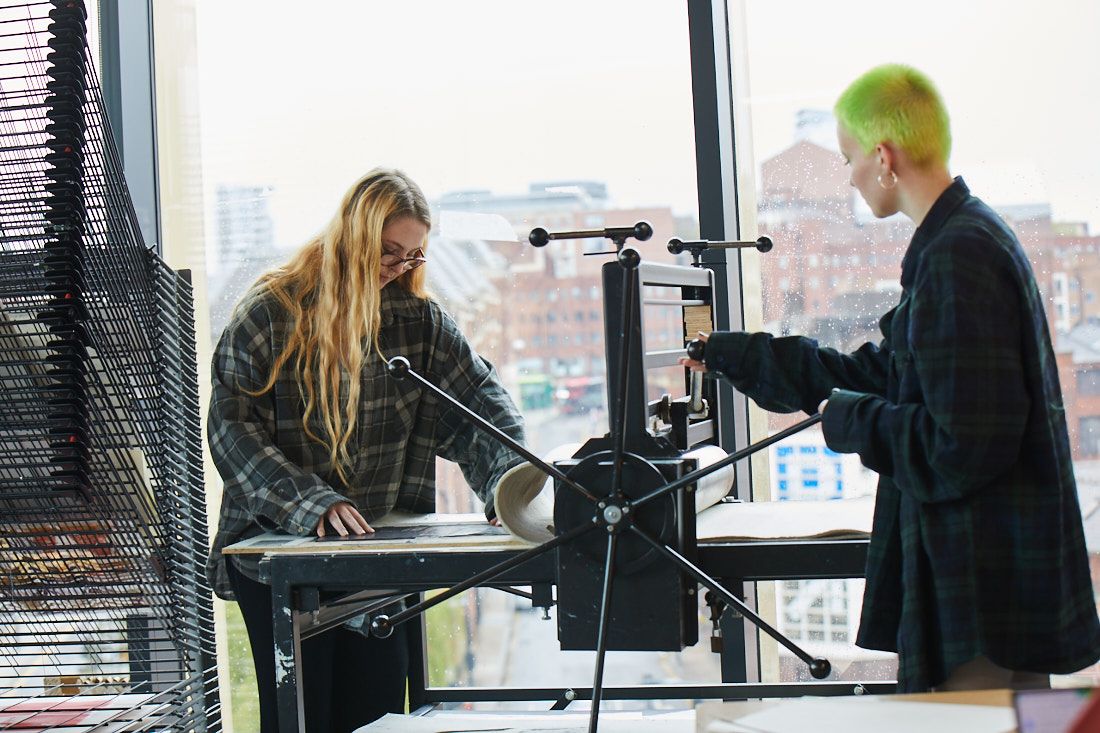 Two creative arts students using a binding machine