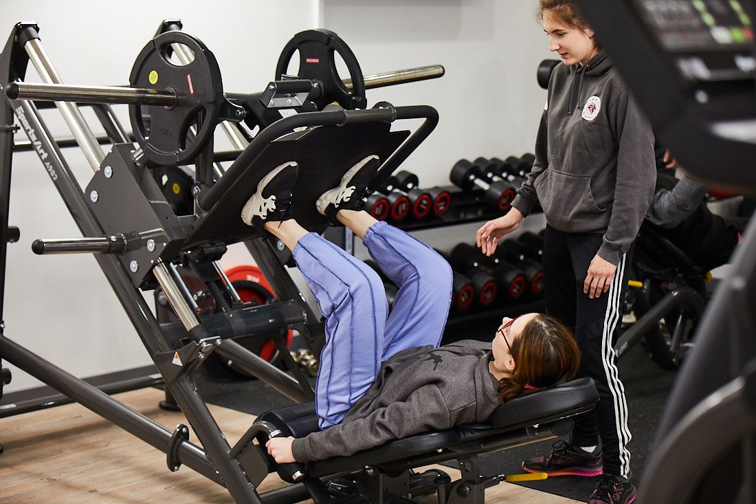 LCC Sports student teaching a fellow female student how to use the leg press machine