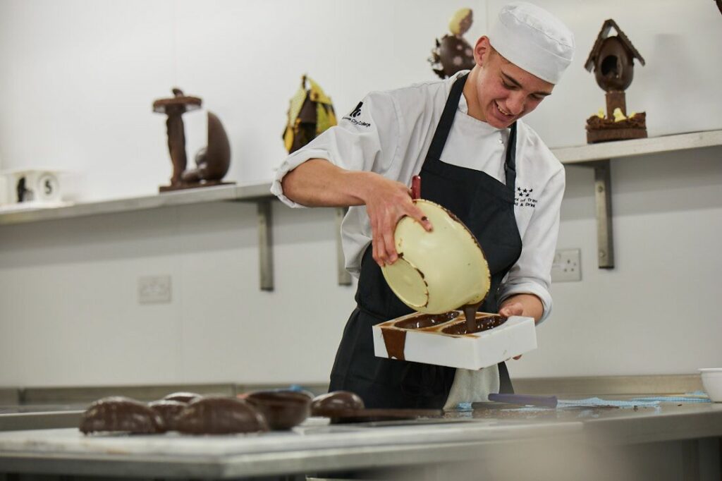 Travel, Food and Drink student pouring melted chocolate into an easter egg mold