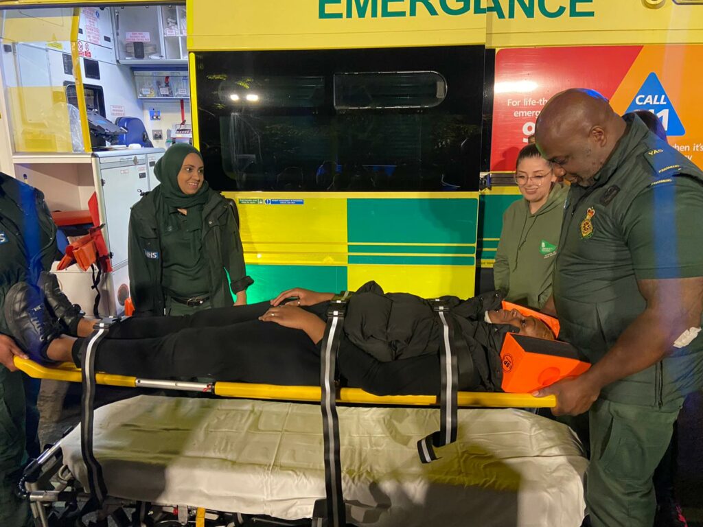 Paramedics wearing green uniform carrying patient on stretcher