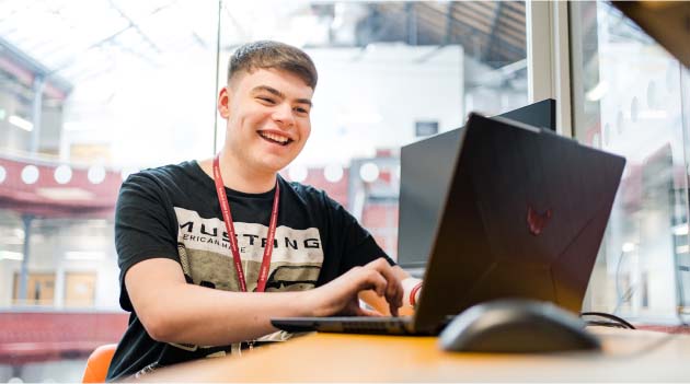 Leeds City College student apprentice sat at desk working on laptop and smiling