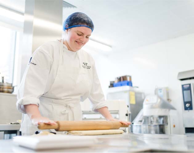 Leeds City College commis chef apprentice in kitchen wearing chef overalls, smiling rolling pastry