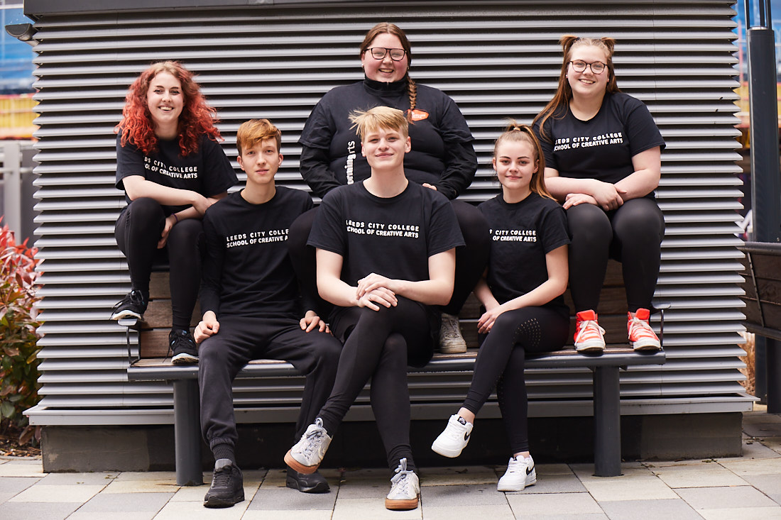 School of Creative Arts students wearing black T-shirt sitting together on a bench smiling