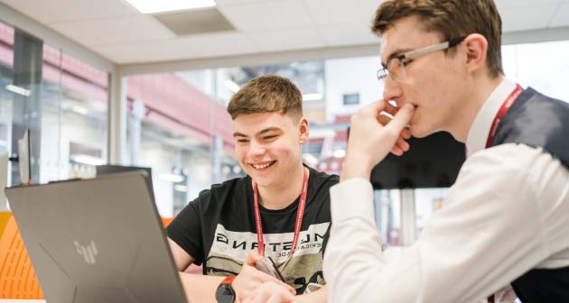 Two students sat looking at laptop, smiling wearing Leeds City College lanyards