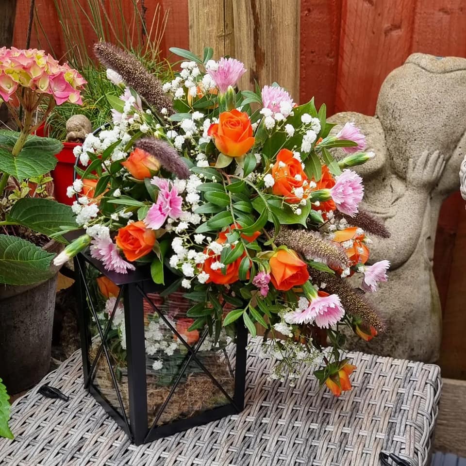 Orange, white and pink flowers on a table in a glass and iron frame