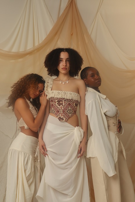 Three women modelling white dresses, some plain, some patterned, stand together side by side