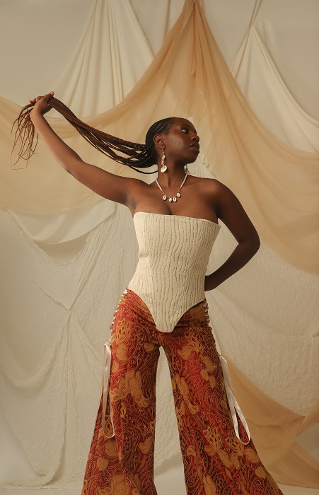 Female model wearing white top and orange wide leg trousers posing for photo