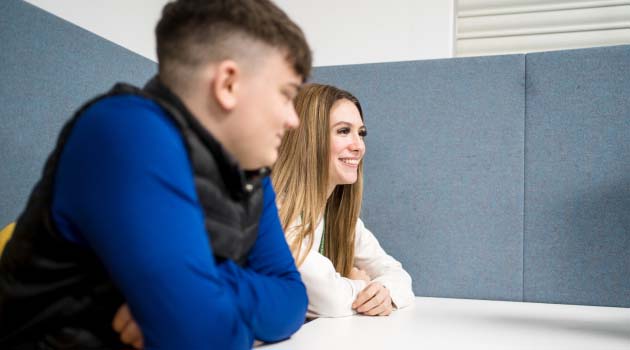 Two students sat at a table smiling with arms folded