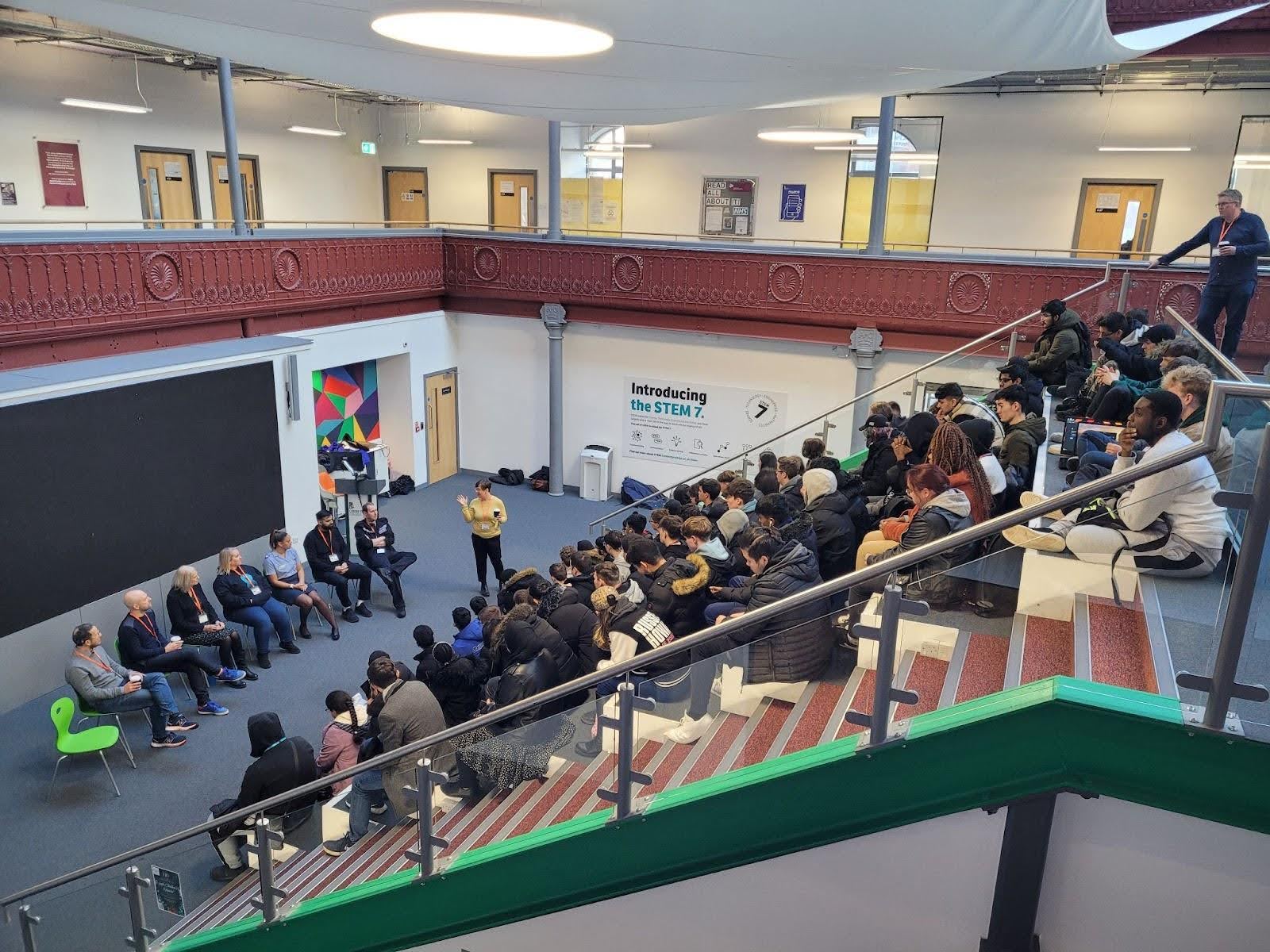 People of different ages and backgrounds sitting on the stairs in a building, engaged in conversation.