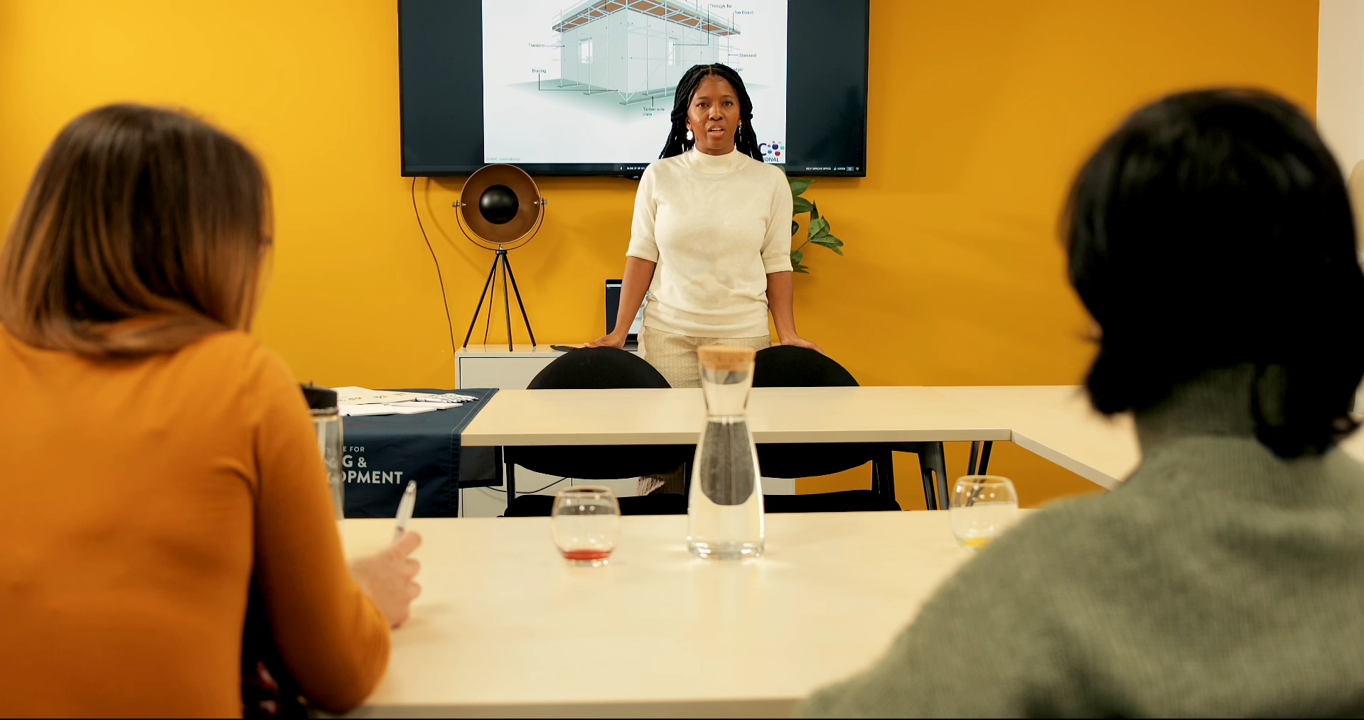 Student wearing white top standing giving presentation in the classroom with big screen on the wall