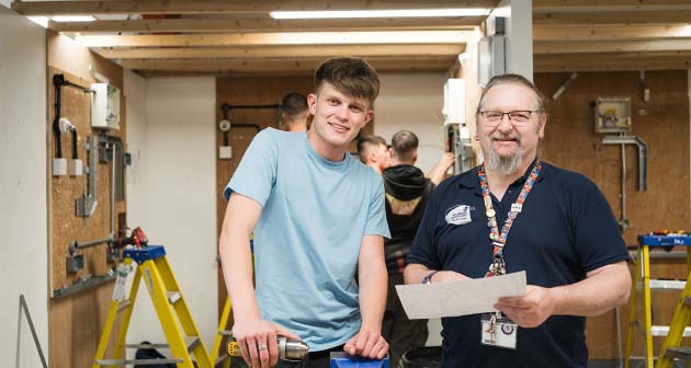 Student stood smiling with teacher in electrical workshop