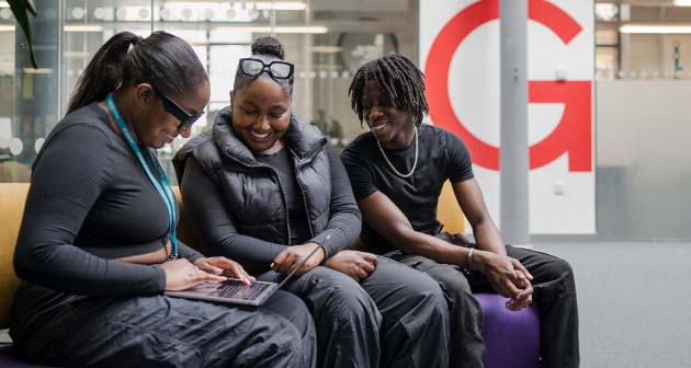 Teacher, parent and student sat down in the Printworks campus looking at a laptop during enrolment