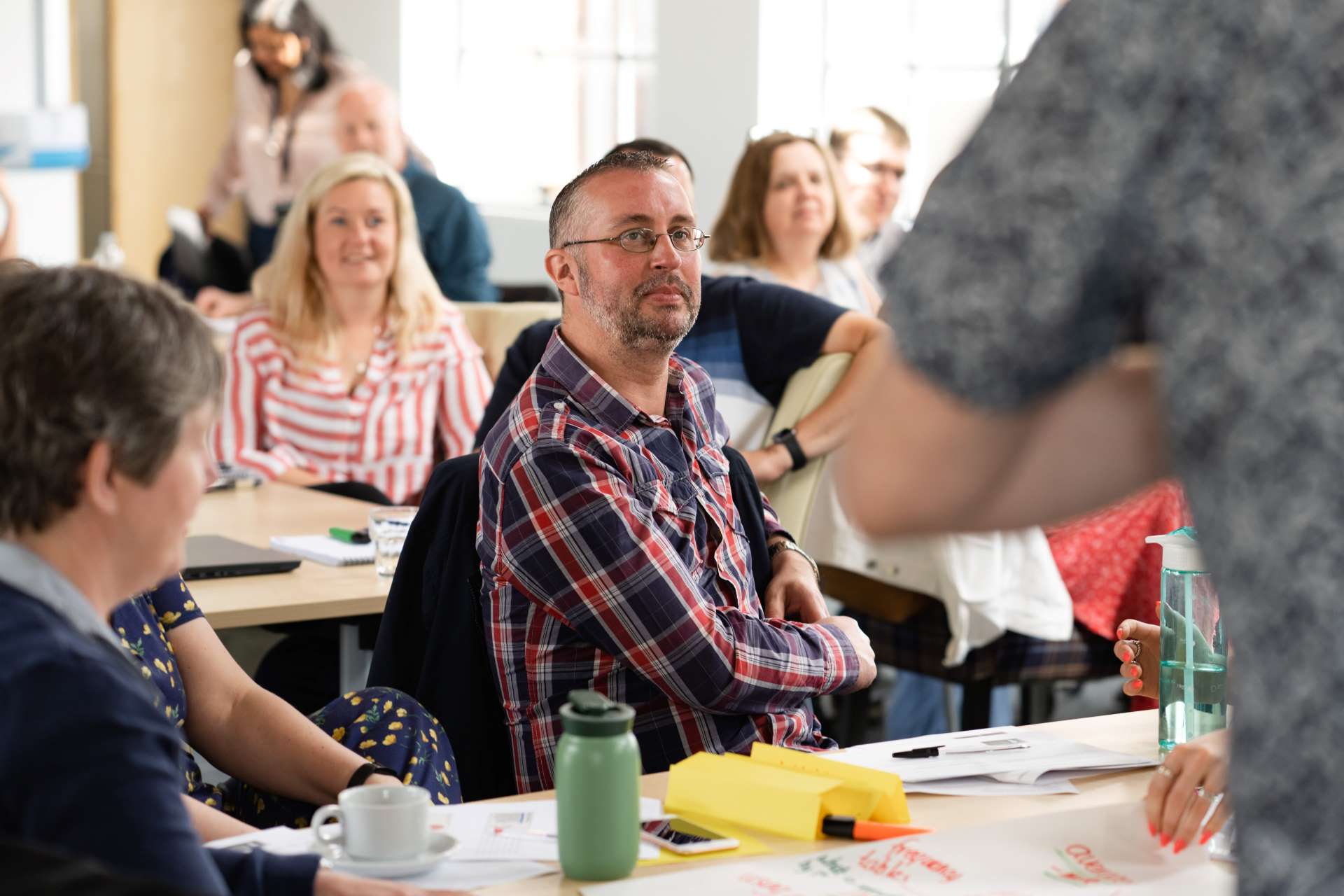 Group of adult learners sat in a glass room with the focus on a man with a checked shirt and glasses