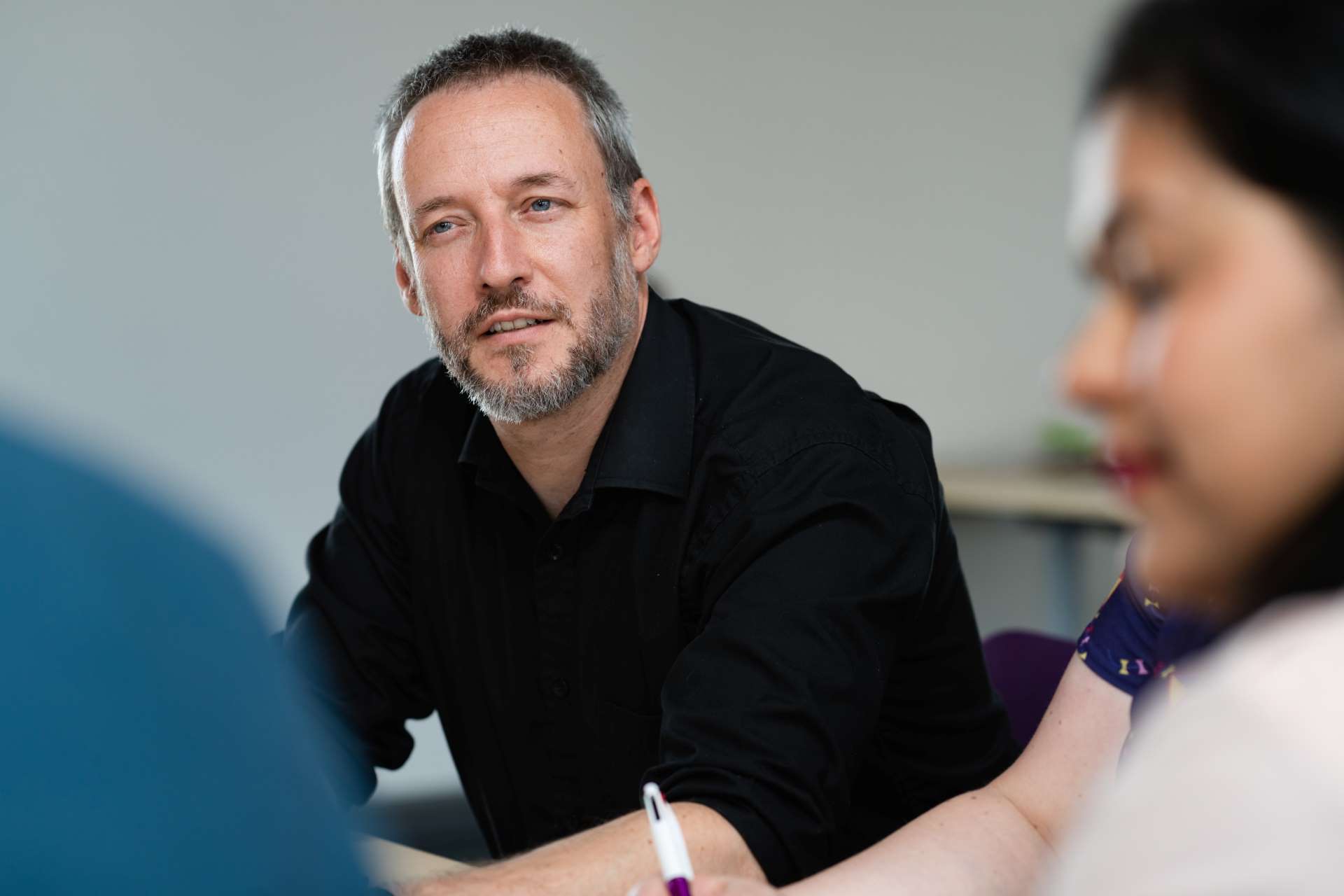 Male adult learner wearing a black shirt with short graying hair and short beard sat down listening