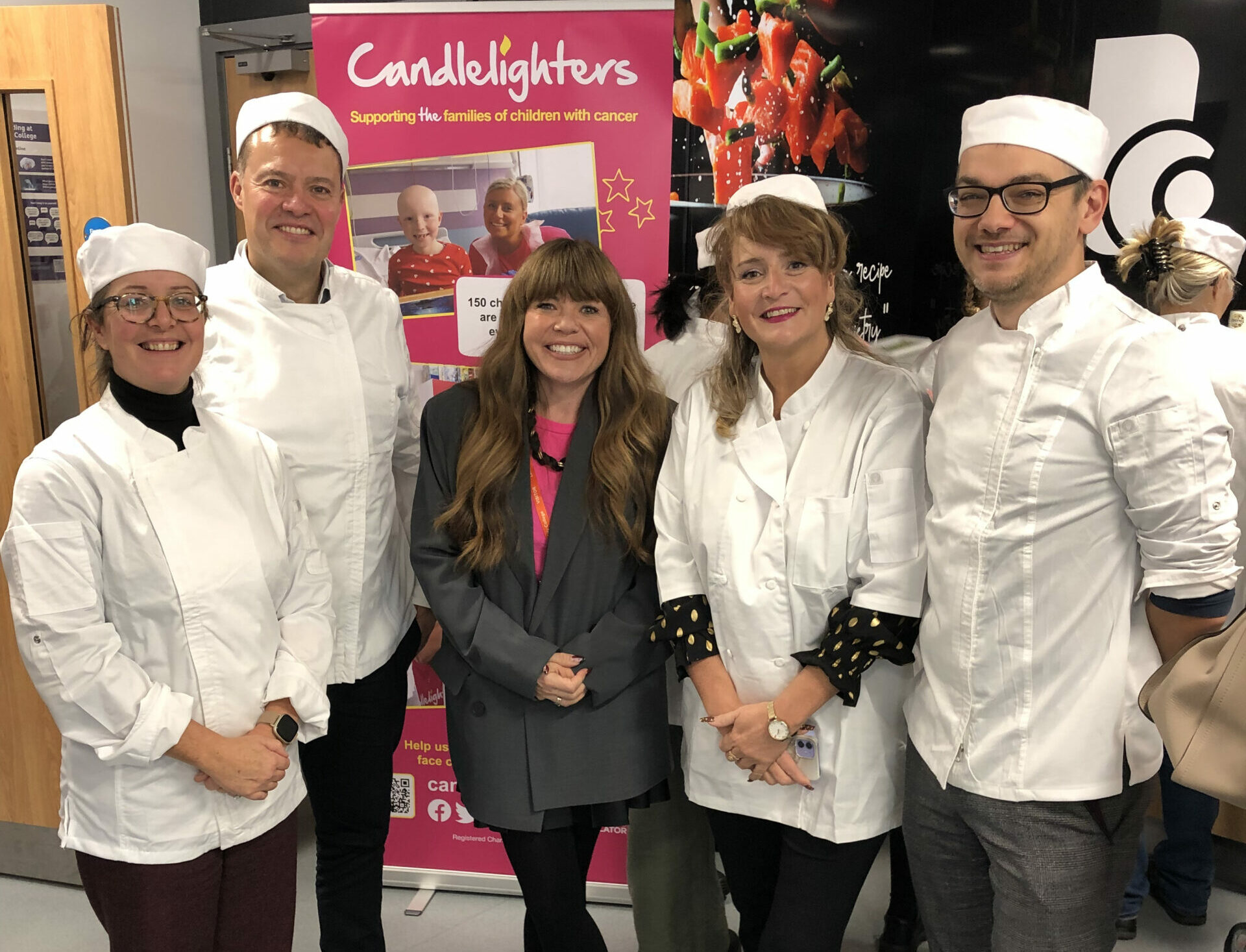 two men and two women in chefs whites stand with a woman in casual clothes.