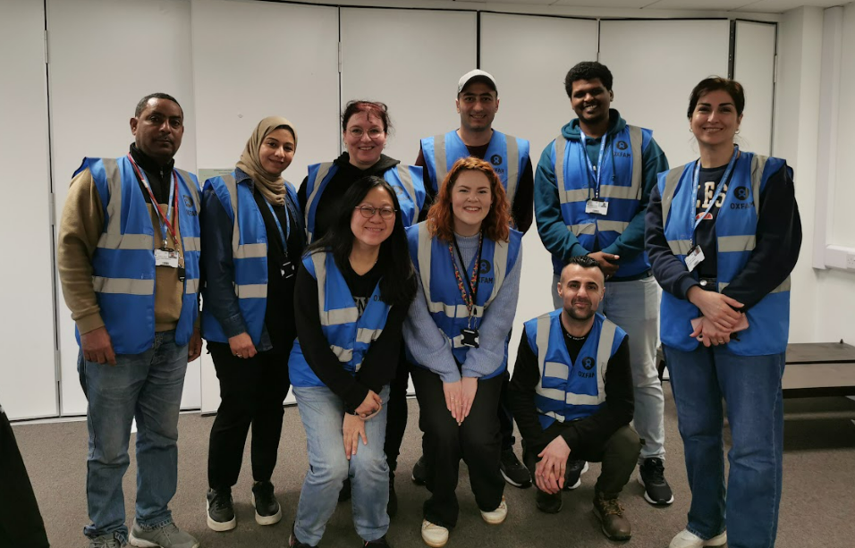 A group of adults wearing blue vests smiles together for a photo.