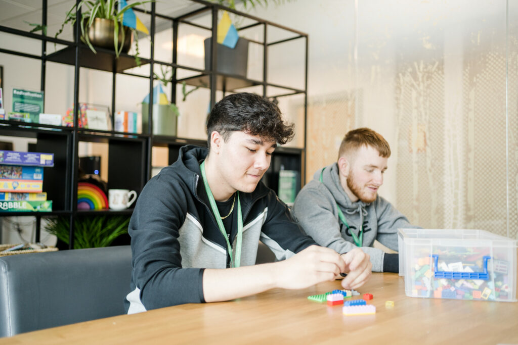 Two young men enjoying a fun time at a table, building with a colorful box of Legos.