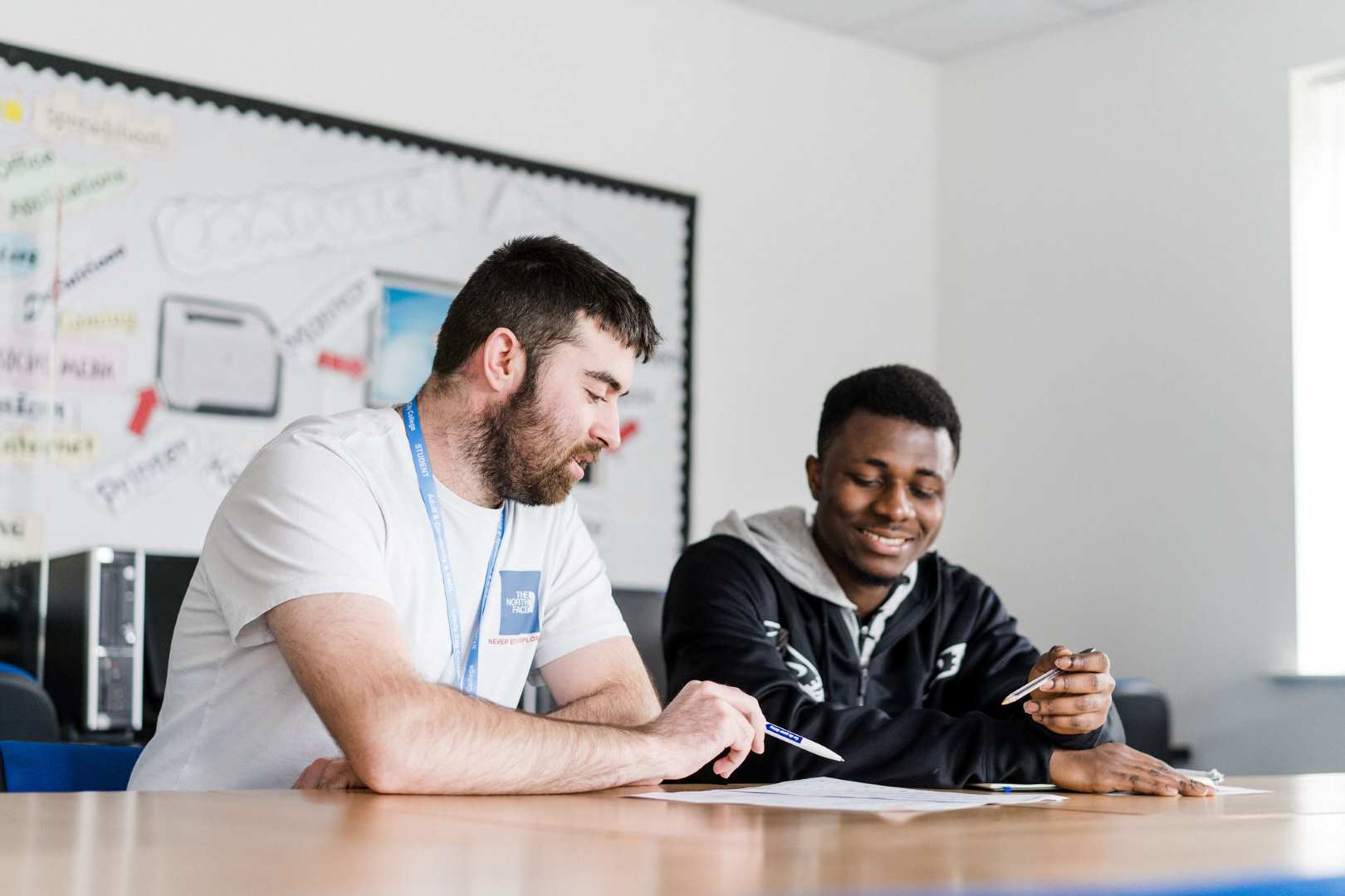 Two adult learners sat together going through a document and holding pens ready to write