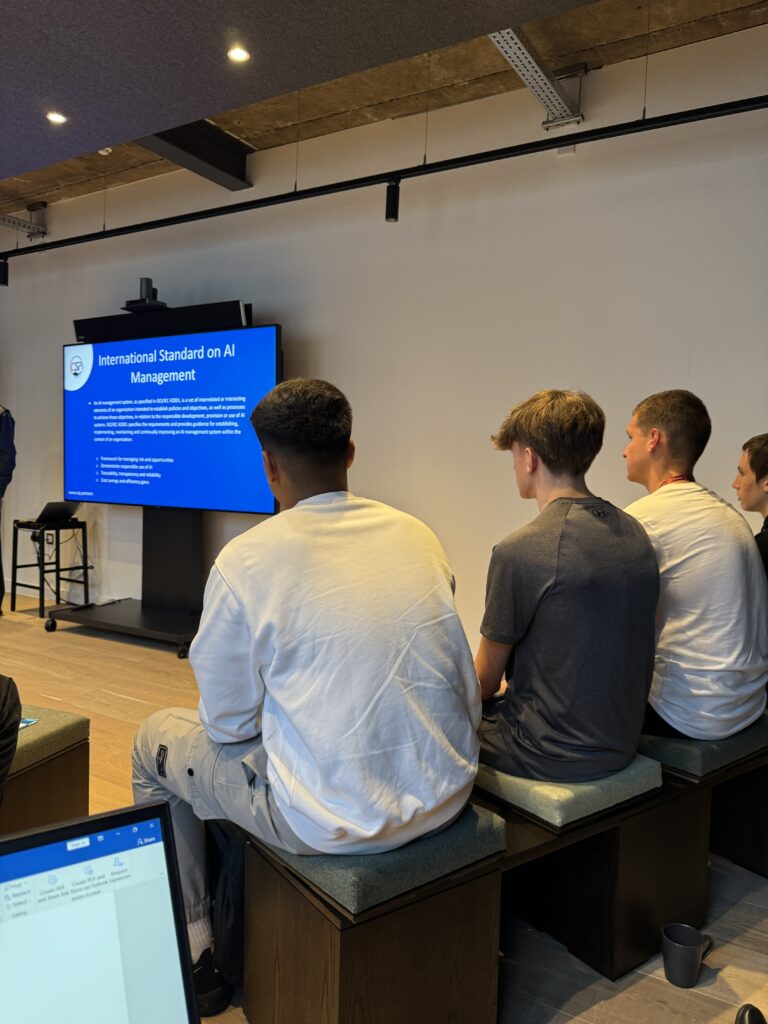 A row of people seated in a room, listening to a presentation.