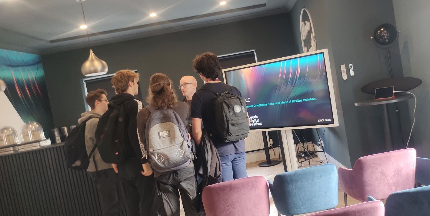 A group of students gathered around a man by a TV screen, engaging in conversation with him