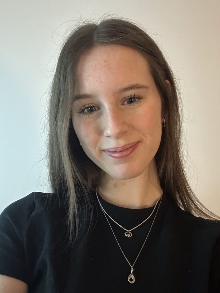 A young woman with long brown hair smiles and poses for the camera