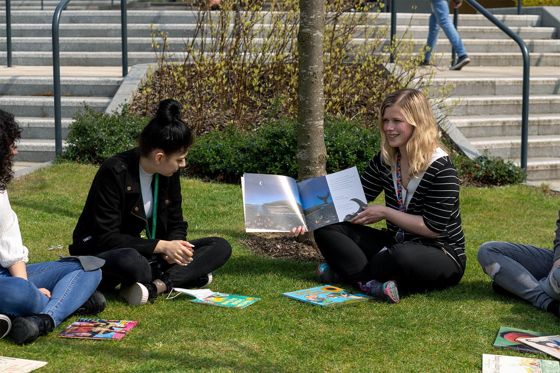 Young people sitting on a lawn with books scattered on the grass