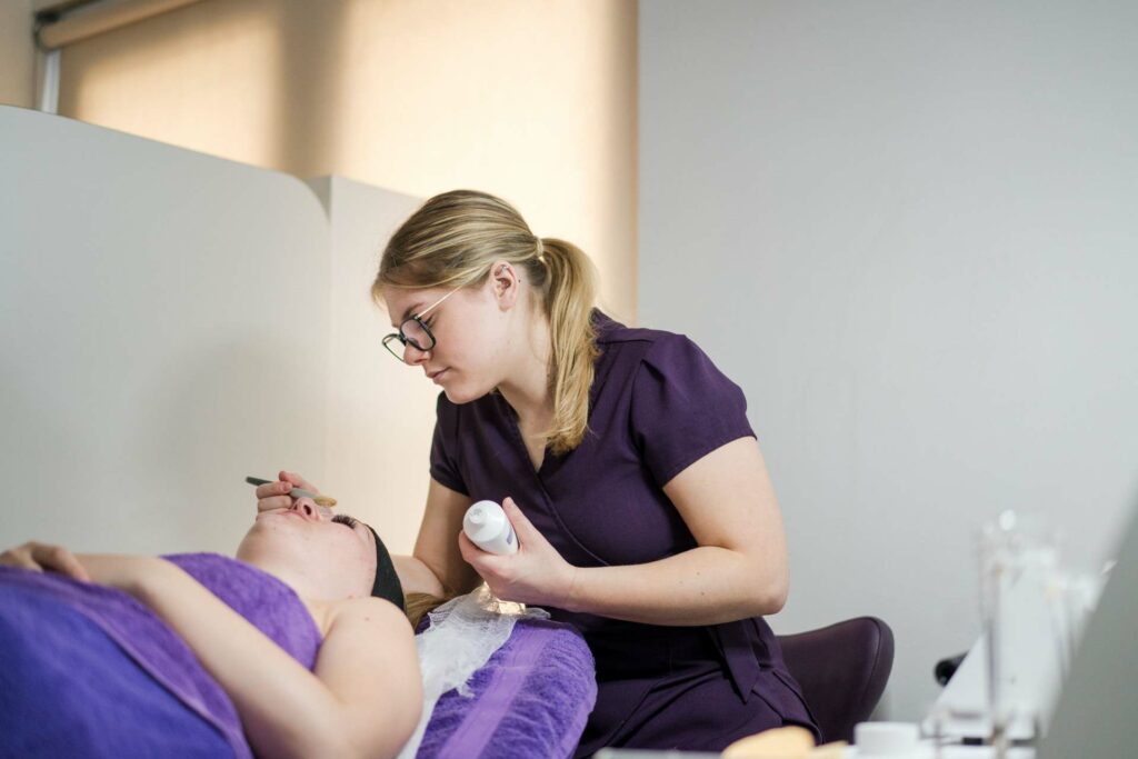 A female student performing a eyebrow waxing treatment to a client