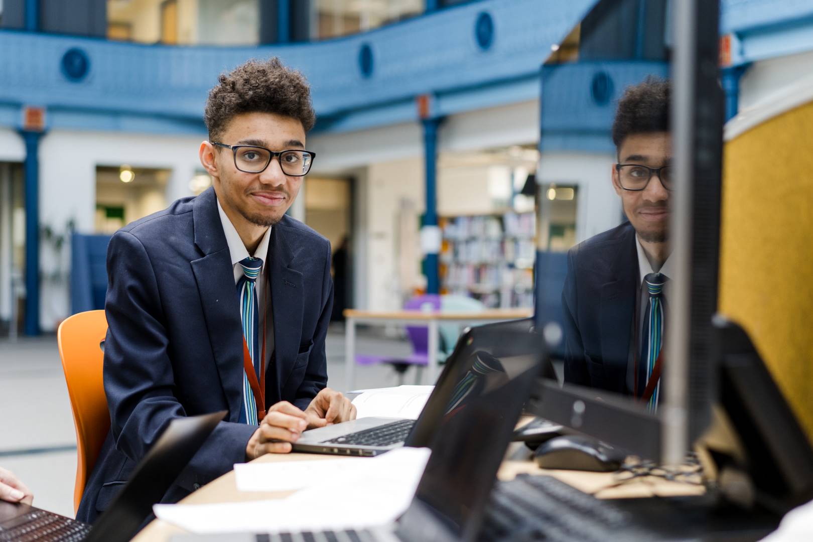 LCC cabin crew student dressed in blue jacket, white shirt and blue stripe tie sitting working on the laptop whilst smiling at the camera