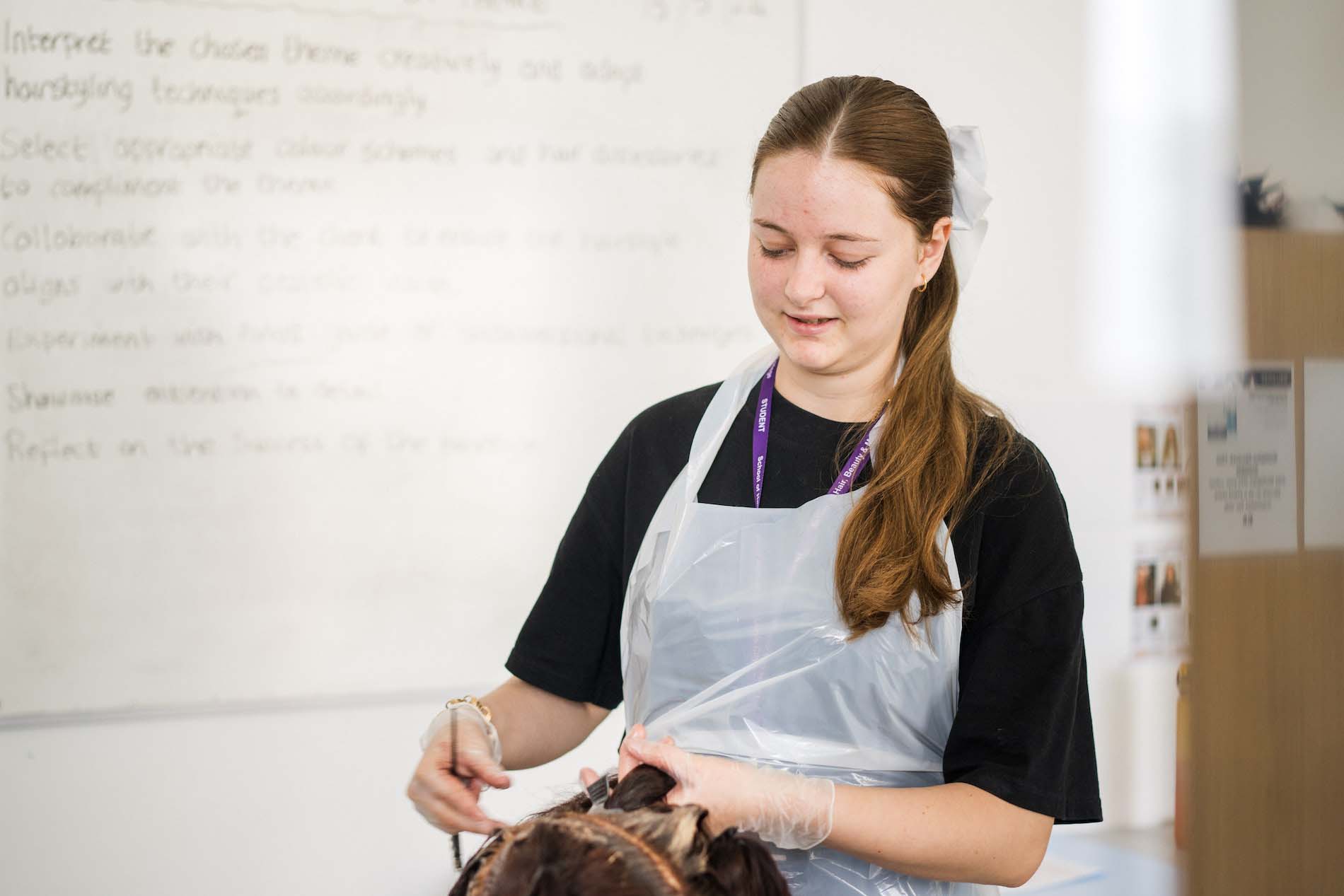 Hairdressing student at Leeds City College Printworks campus wearing an apron whilst learning to apply hair colour