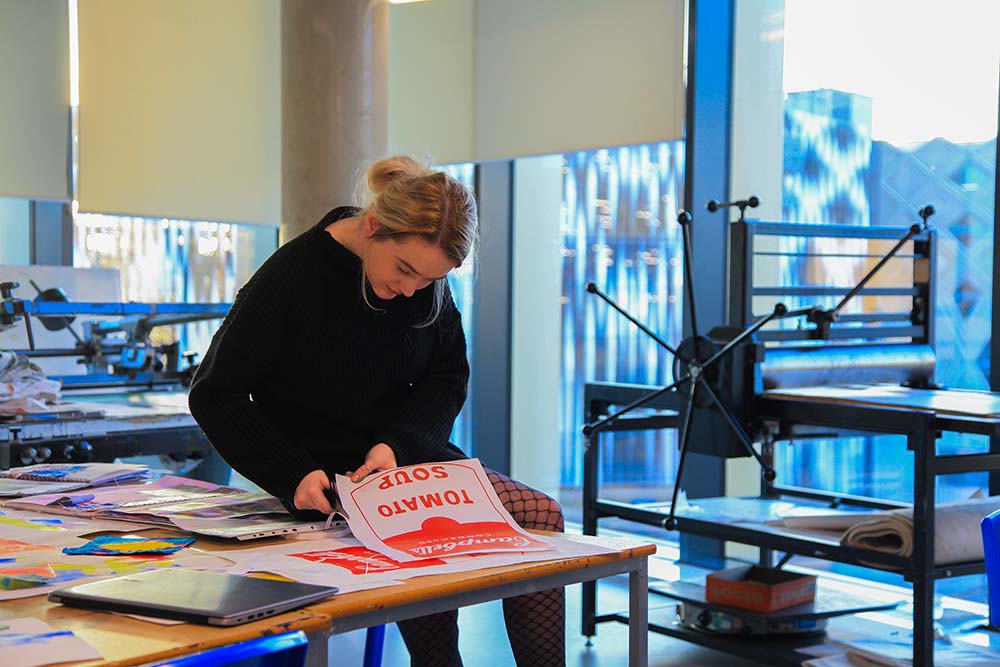 Creative Arts Art and Design student in workshop cutting out a screen print of Campbells tomato soup