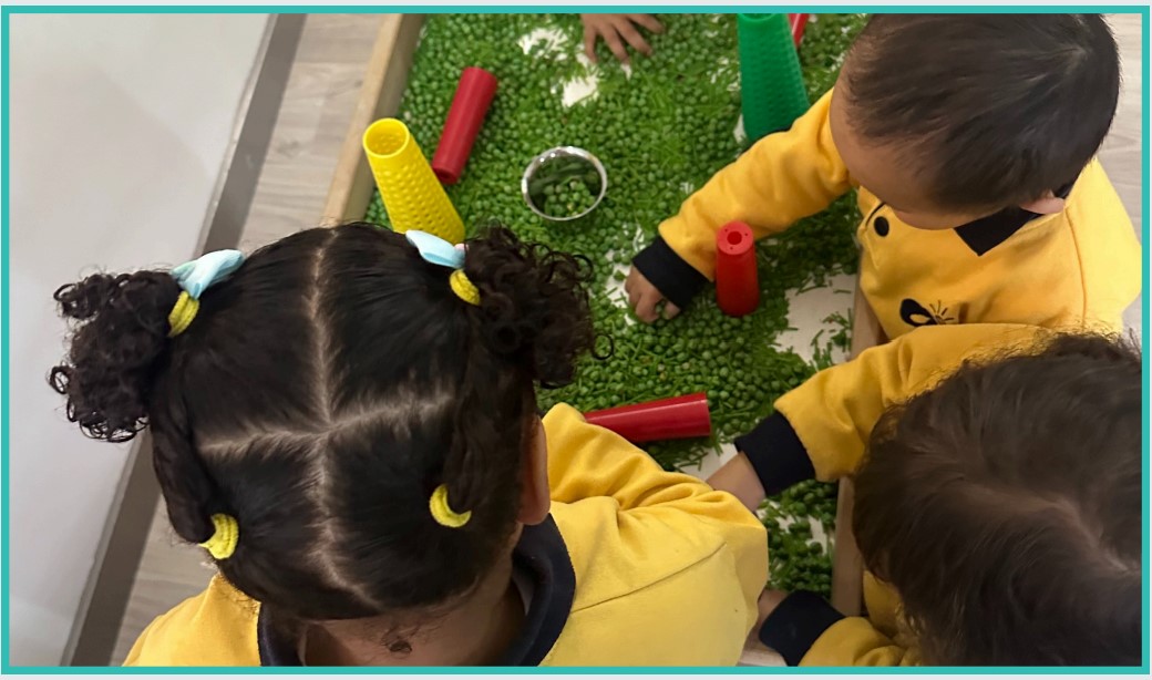 Toddlers playing with peas in a sensory class wearing yellow nursery tops