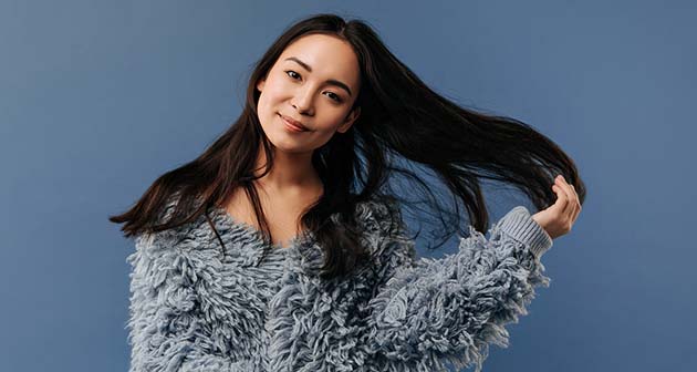 Model wearing grey fluffy top putting hand through dark brown long hair smiling at camera