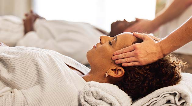 Two people lying back in spa dressing gowns with eyes closed having a head massage