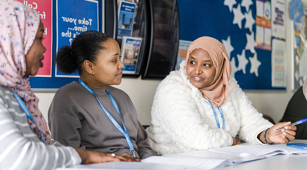 Three adult learners talking sat down in the Enfield Centre building