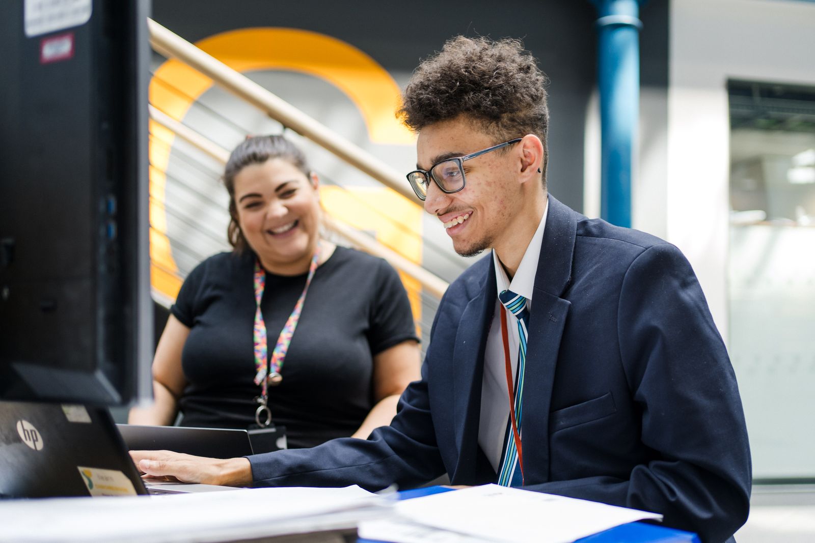student at a computer working, the teacher is looking on