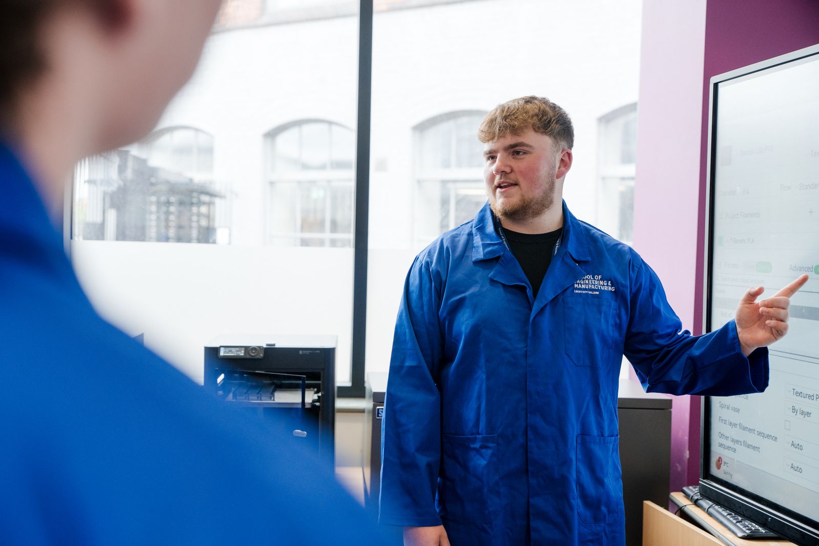 Student wearing blue overalls going through a presentation he is delivering to his peers