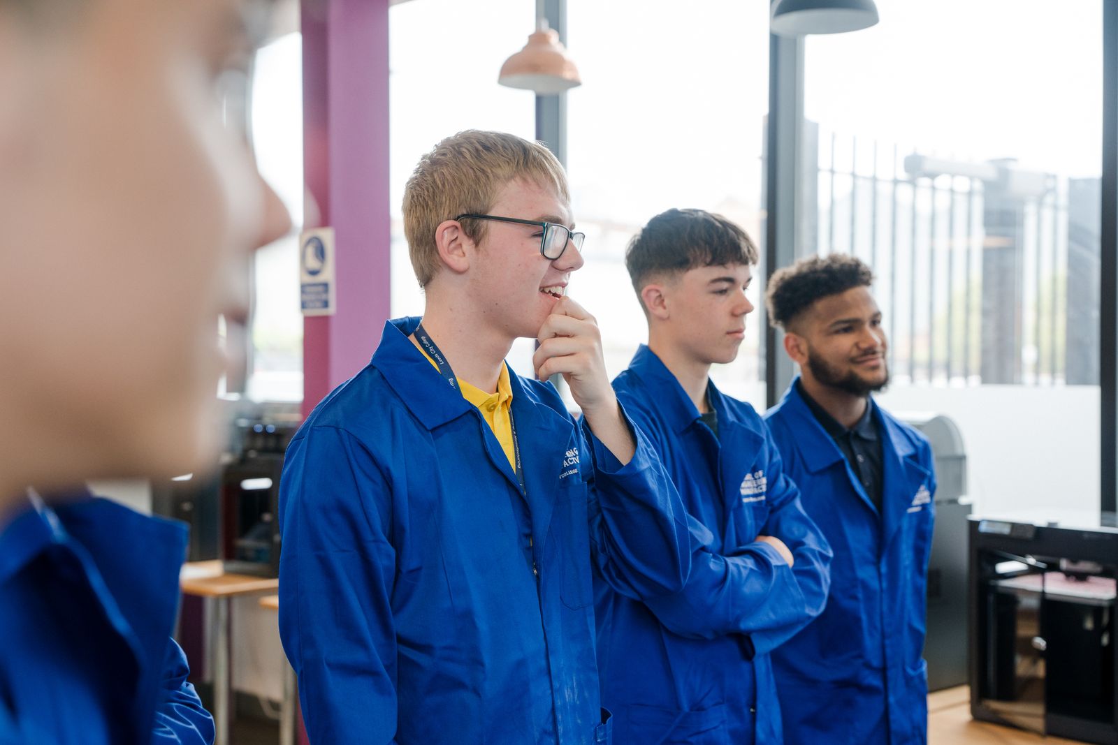 Four students in their work gear listening in the workshop