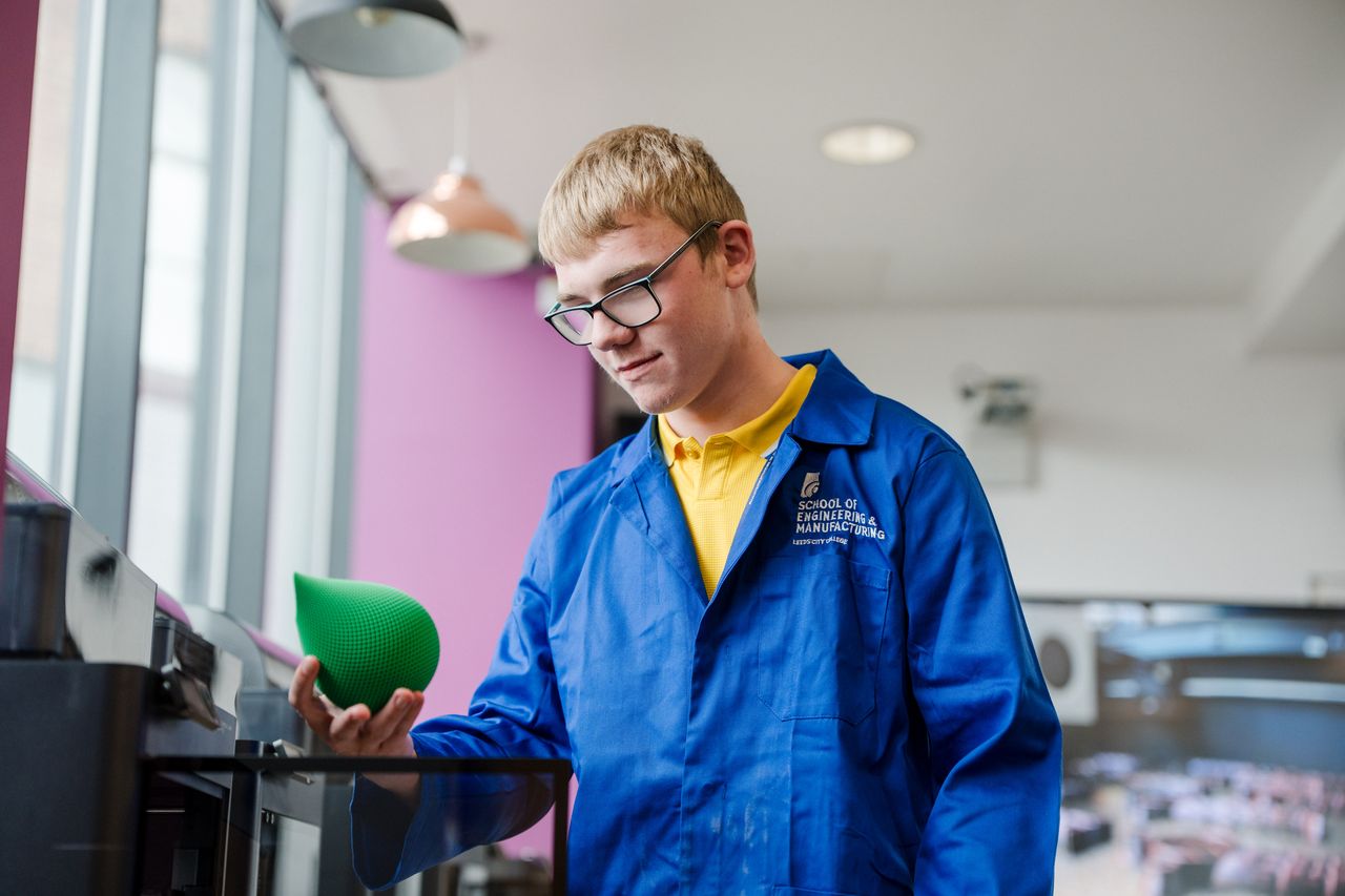 Student wearing their blue overalls holding a 3d printed object they just made