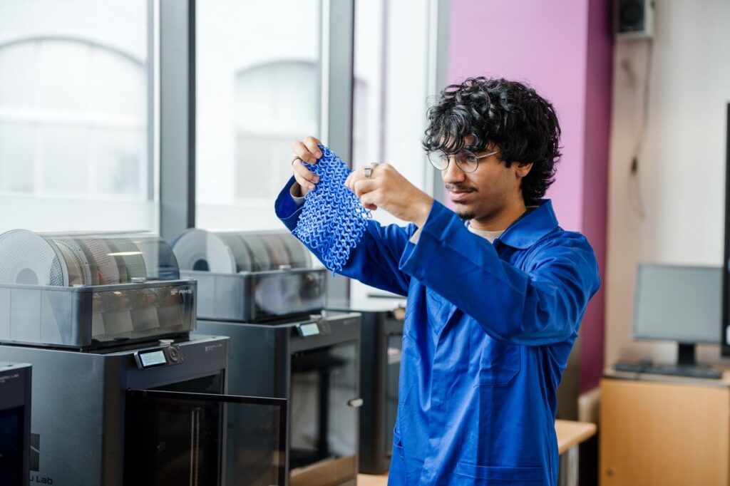 Student wearing their blue overalls holding a plastic mesh they have just 3d printed