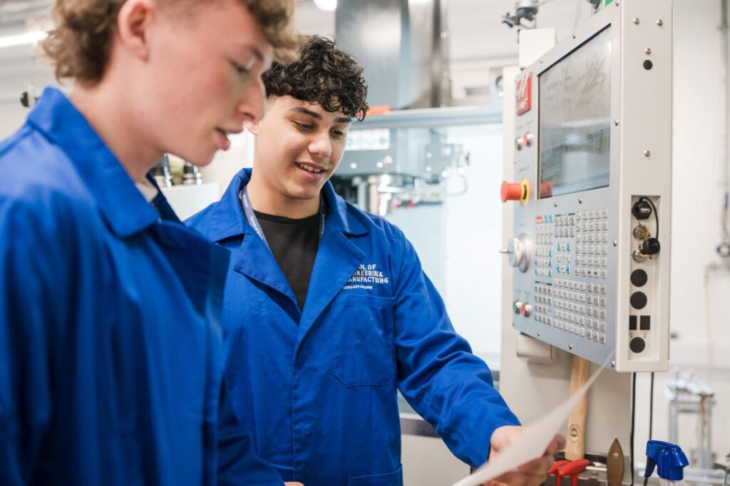 Two students working on machinery reading a note on what they need to create