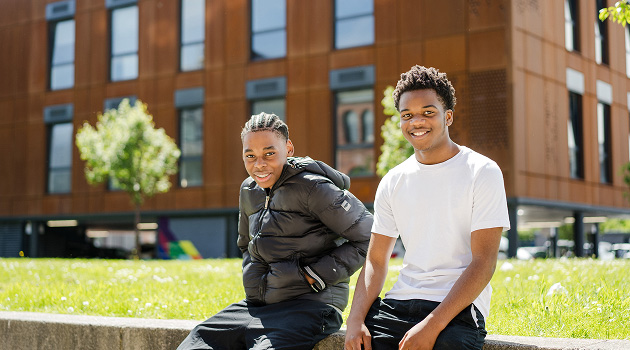 Two students sat on grassy bank outside Leeds City College in the sun smiling