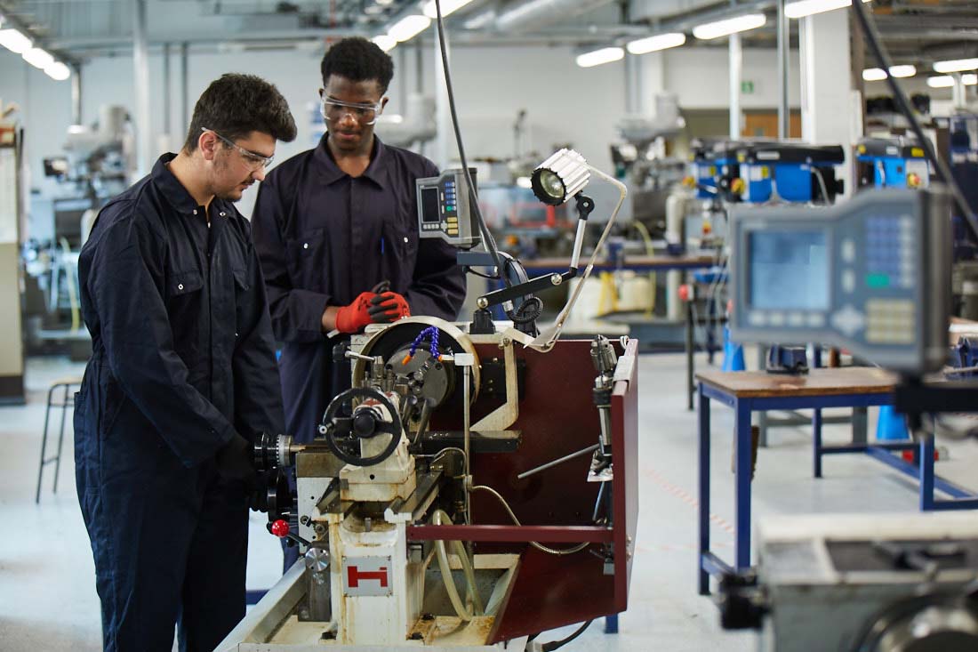 Leeds City College students in overalls and goggles working on engineering and manufacturing equipment in workshop