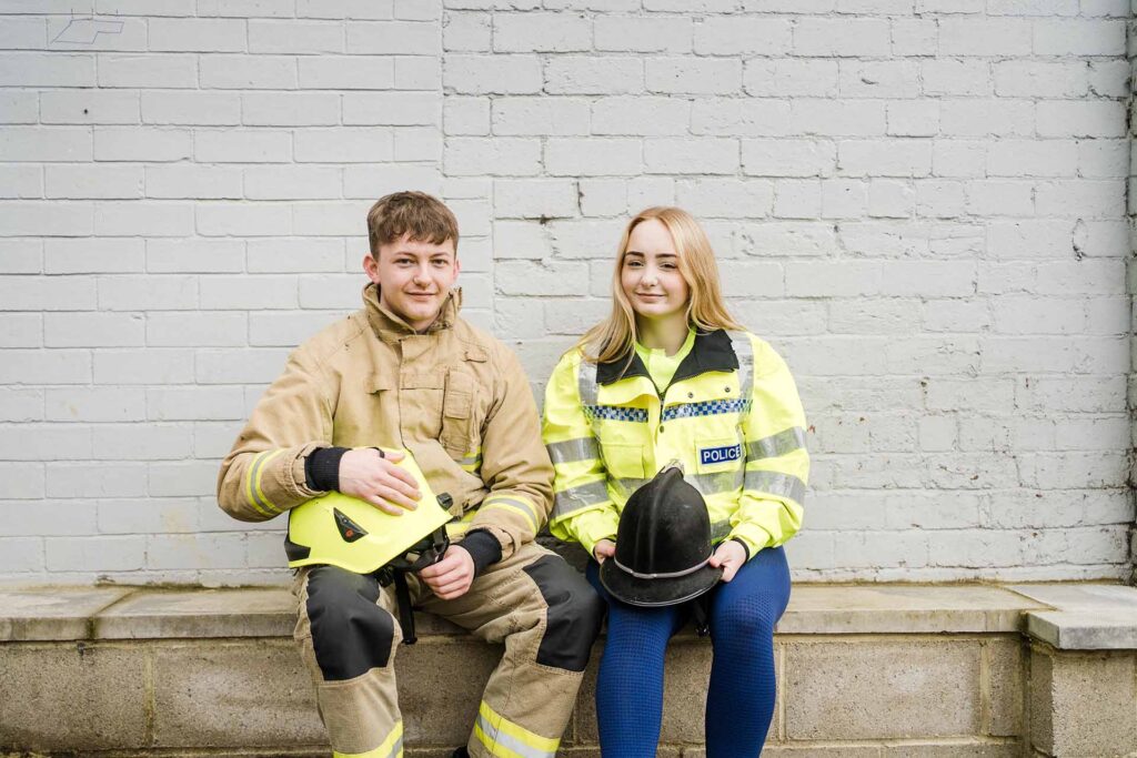 A male student wearing firefighting uniform sitting next to a female student wearing police uniform smiling
