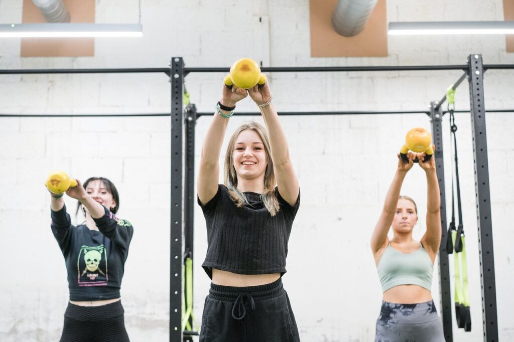Three female students in the gym doing kettlebell raises